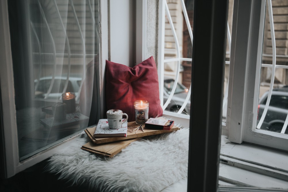 Cozy window sill with candle, books, and pillow.