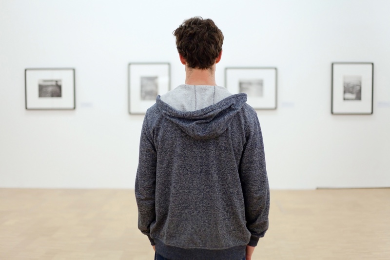 A man in a hoodie admiring artwork in a gallery.