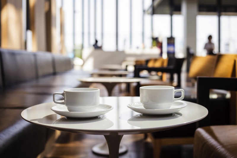 Two coffee cups on a wooden table inside a coffee shop.