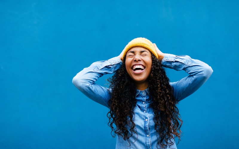 A woman with long curly hair smiling and laughing joyfully.