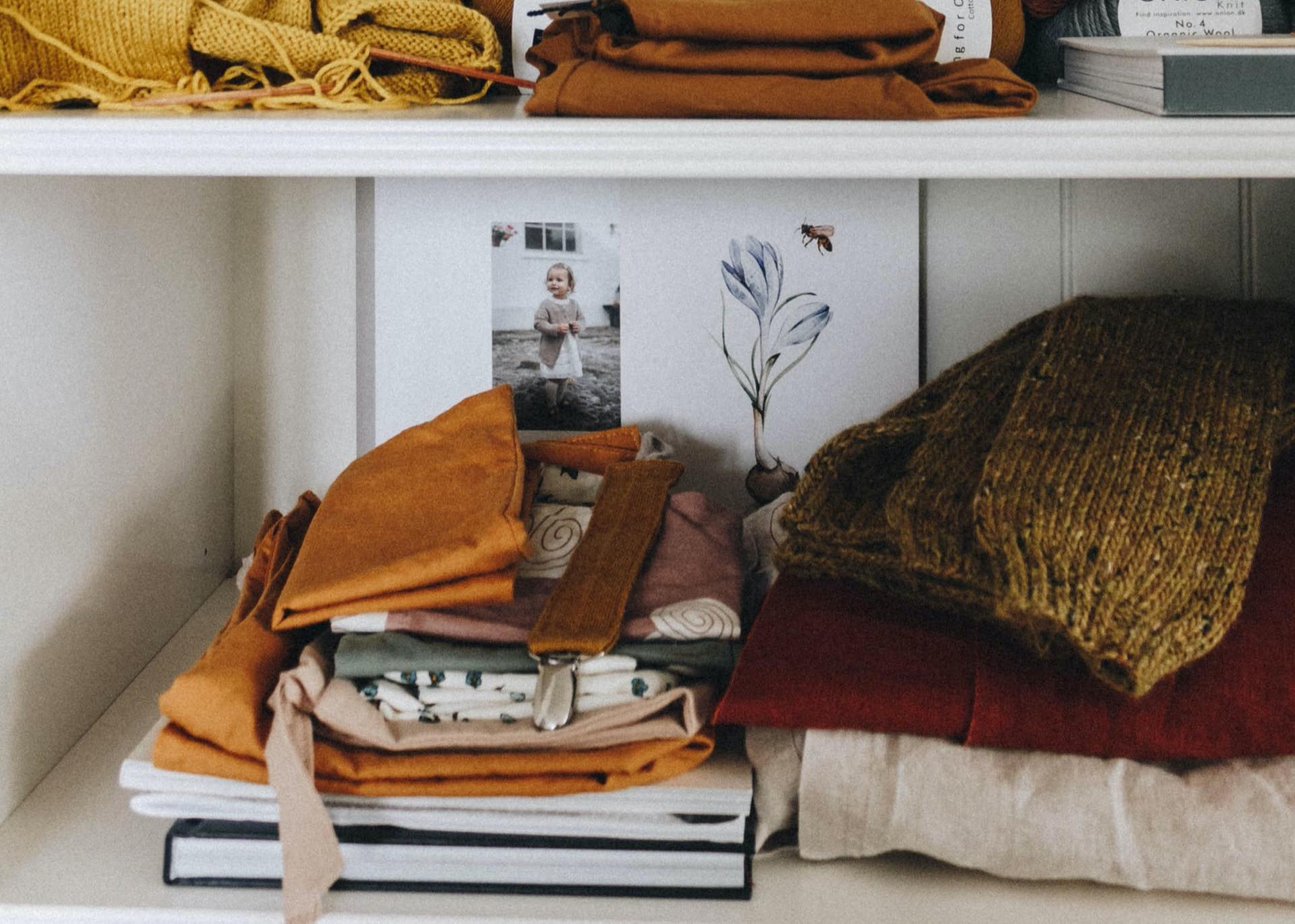 Assorted clothes and books on a white shelf.