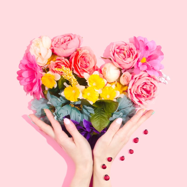 A woman's hand holding a heart-shaped bouquet of flowers.