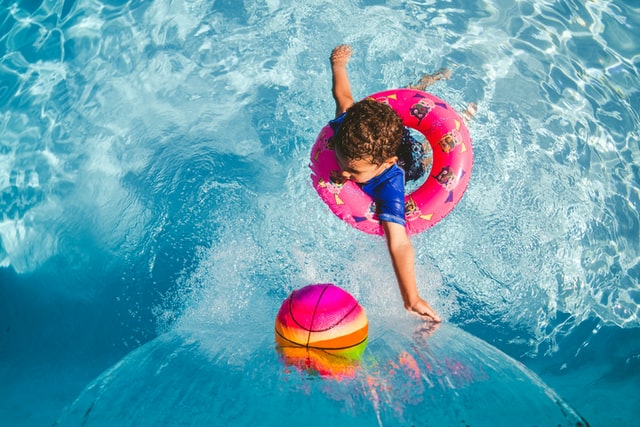 A child happily playing in a pool with a ball and a life ring.