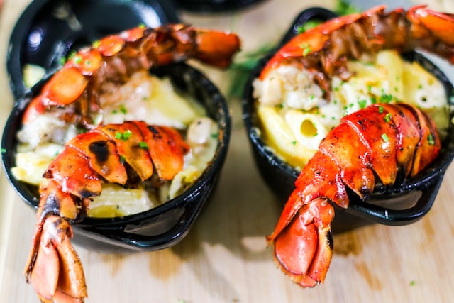 A gourmet meal with two lobster tails in black bowls topped with cheese.