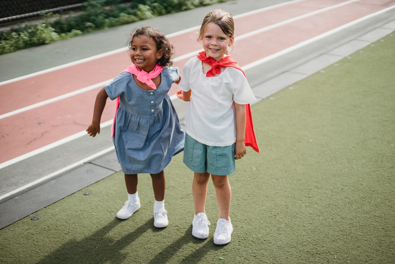 Two young girls in colorful capes standing on a track.