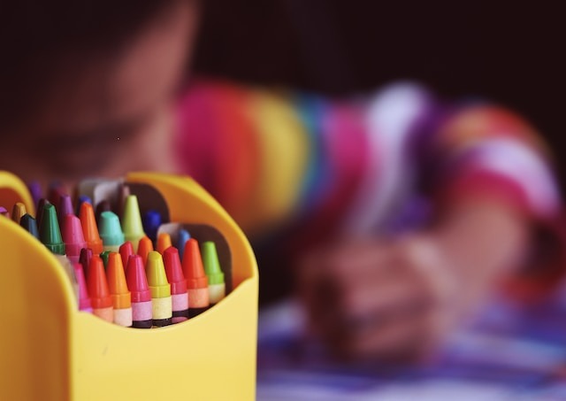 A box of crayons with a blurred kid at the background.